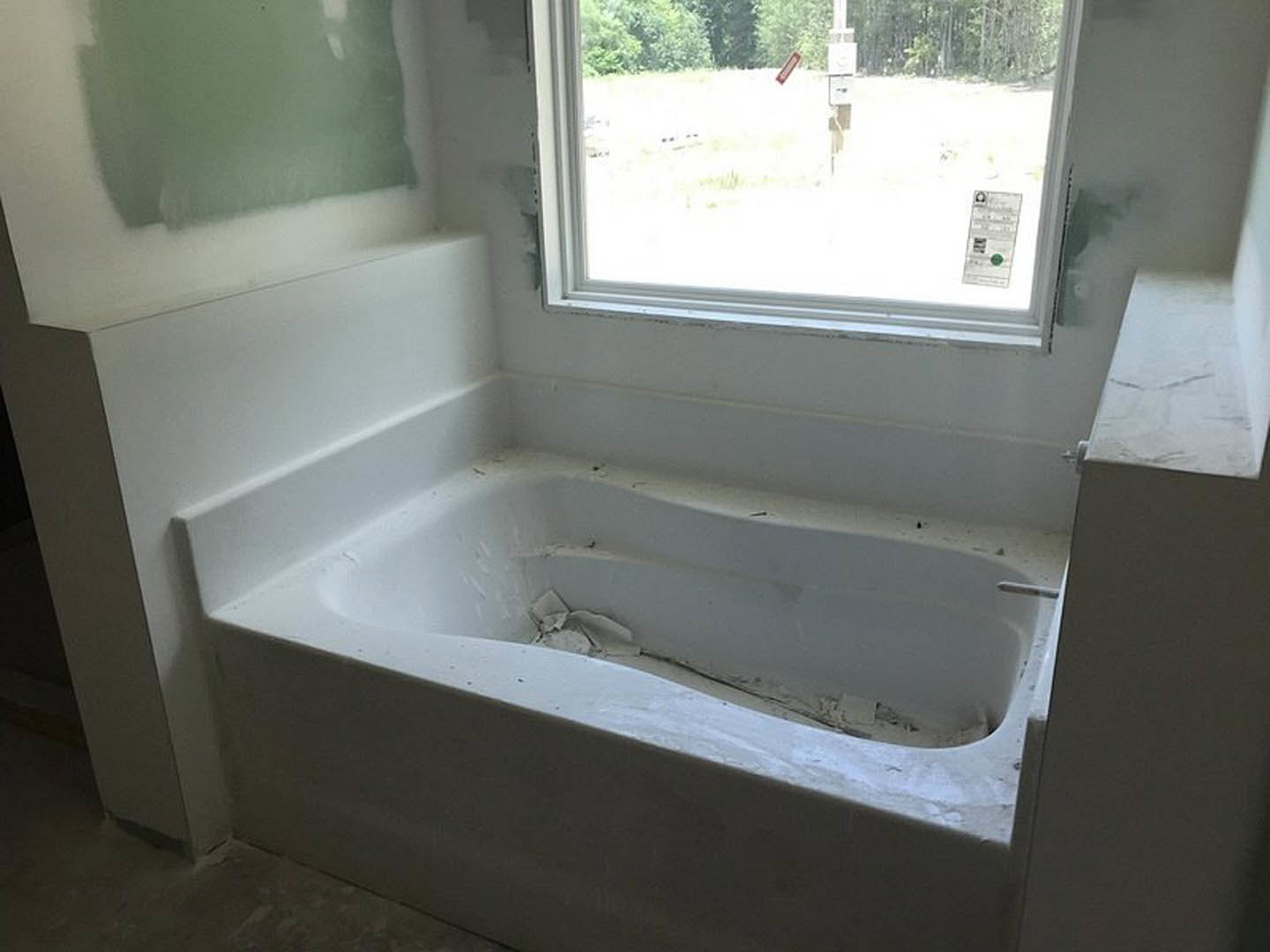 White freestanding bathtub with peeling paint beside a window, white column, and neutral walls in a residential bathroom