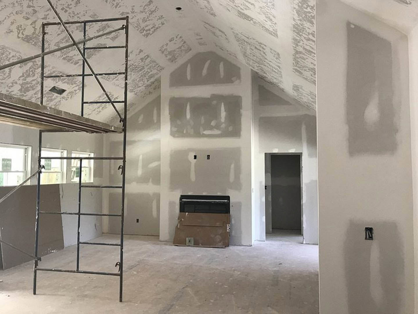 Scaffolding set up in a partially finished room with a modern black fireplace, plaster walls, and large windows