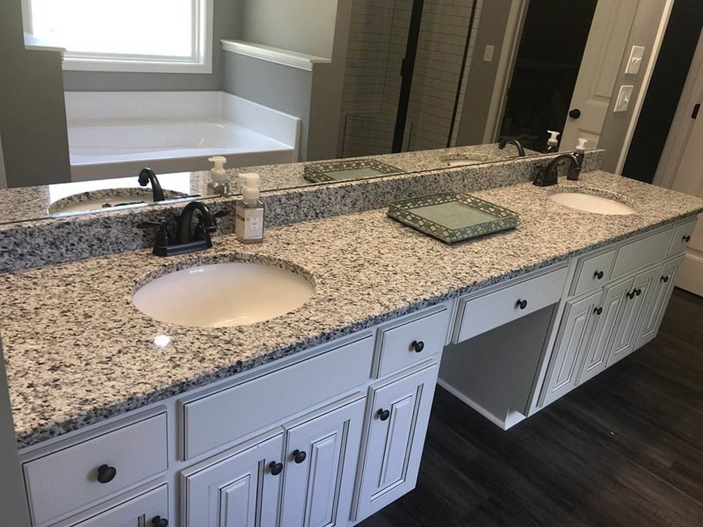 Marble bathroom countertop with white oval sink, chrome faucet, decorative soap bottle, and white cabinetry against a light wall