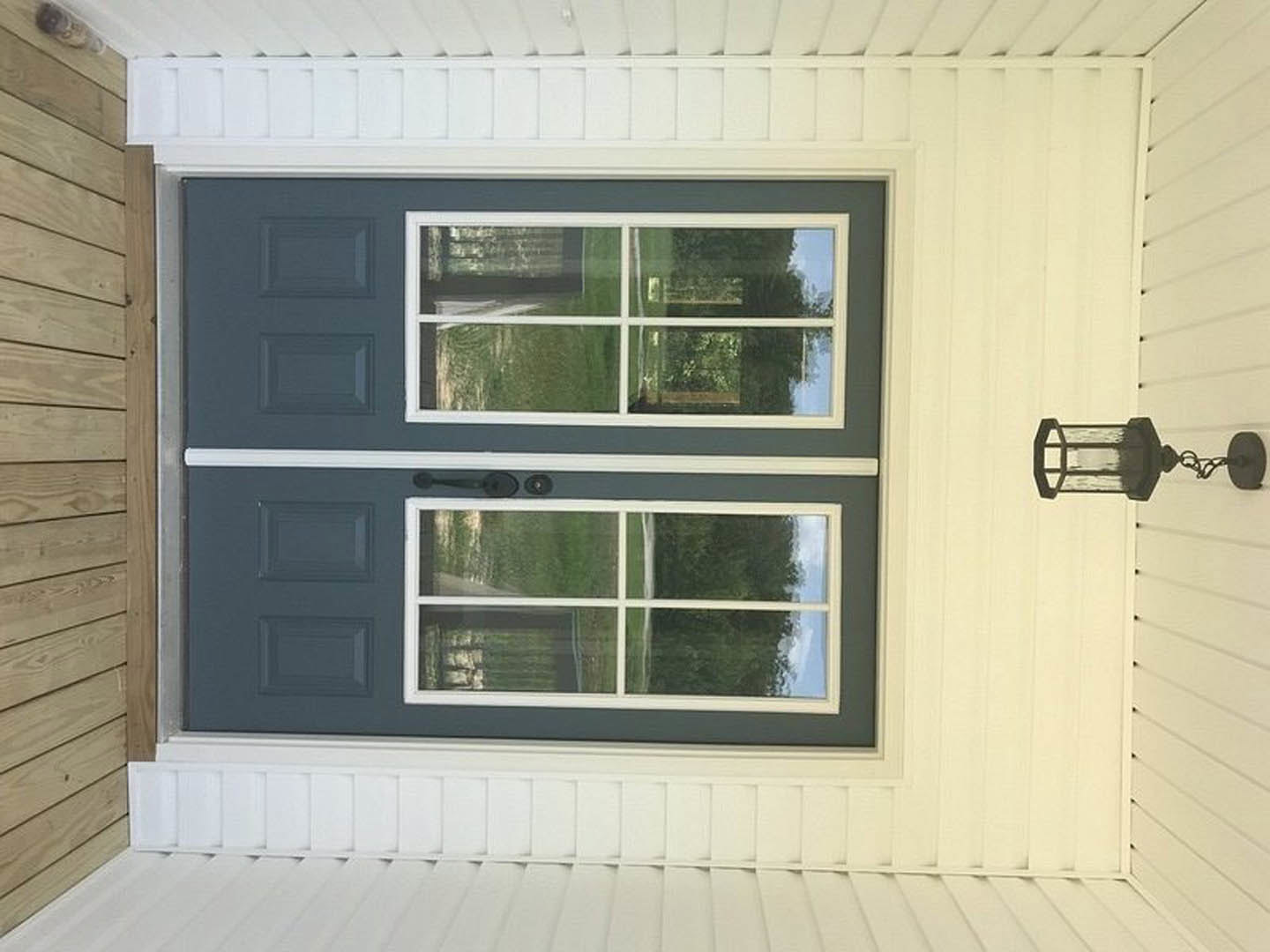 Wood front door with glass window panels, white trim, and black metal lantern light fixture mounted on exterior wall