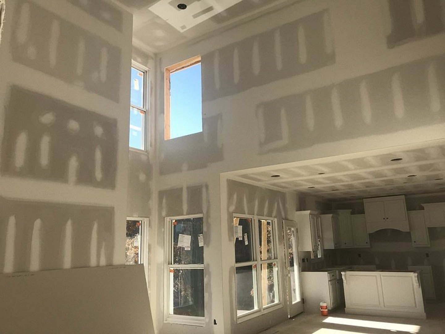 Bright room with white plaster walls, large windows showing blue sky, white cabinet with black handle, glass surface holding a sheet of paper, decorative molding along ceiling and