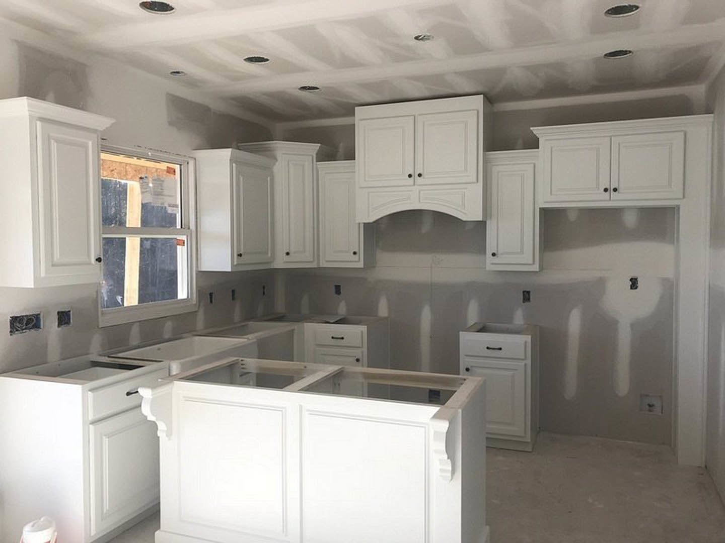 White kitchen with shaker cabinets, stainless steel appliances, quartz countertops, farmhouse sink beneath a large window, and light wood flooring