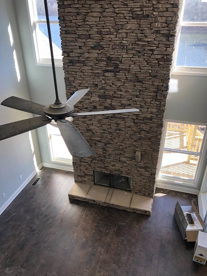 Ceiling fan mounted above a living room with brick fireplace, hardwood floors, and glass door letting in daylight