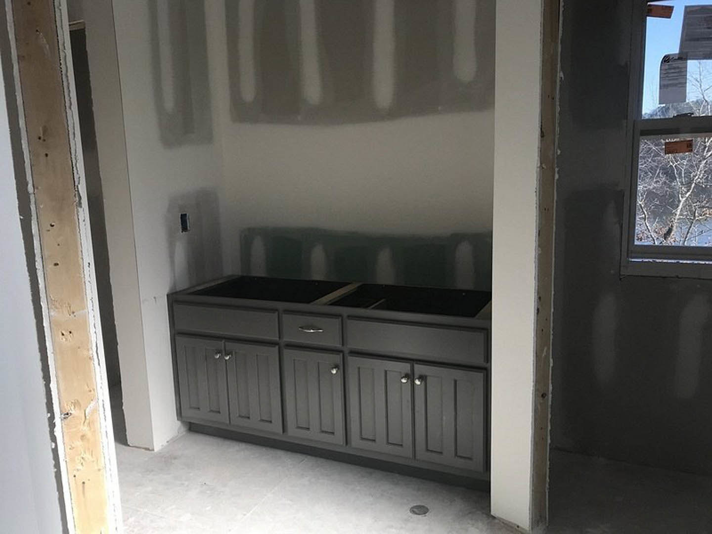 Black kitchen cabinets with sleek hardware, white countertop, stainless steel sink, large window above the workspace, light-colored walls, and drawers integrated into cabinetry