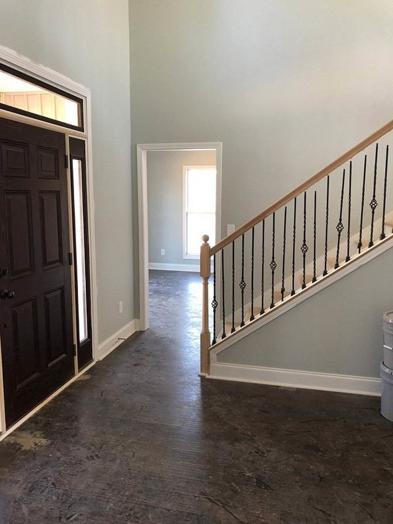 Hallway featuring dark wood flooring, staircase with metal railings, white plaster walls, and a door near a window illuminated by natural light