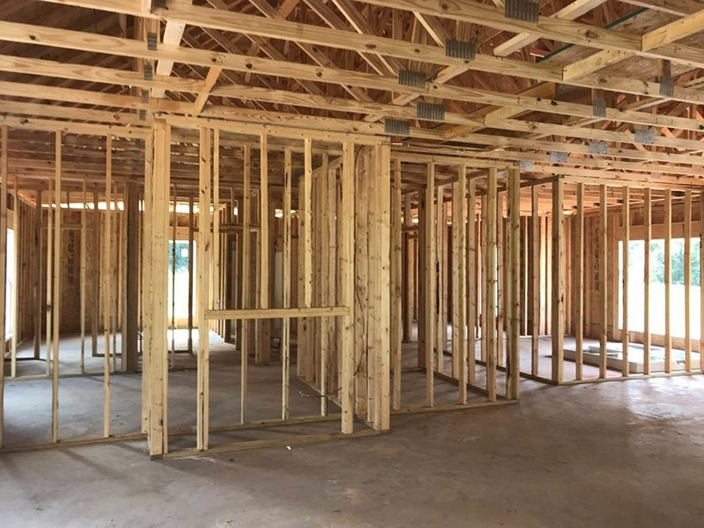 Exposed wooden framing and beams with metal studs, unfinished ceiling and floor, window opening allowing natural light into the construction interior