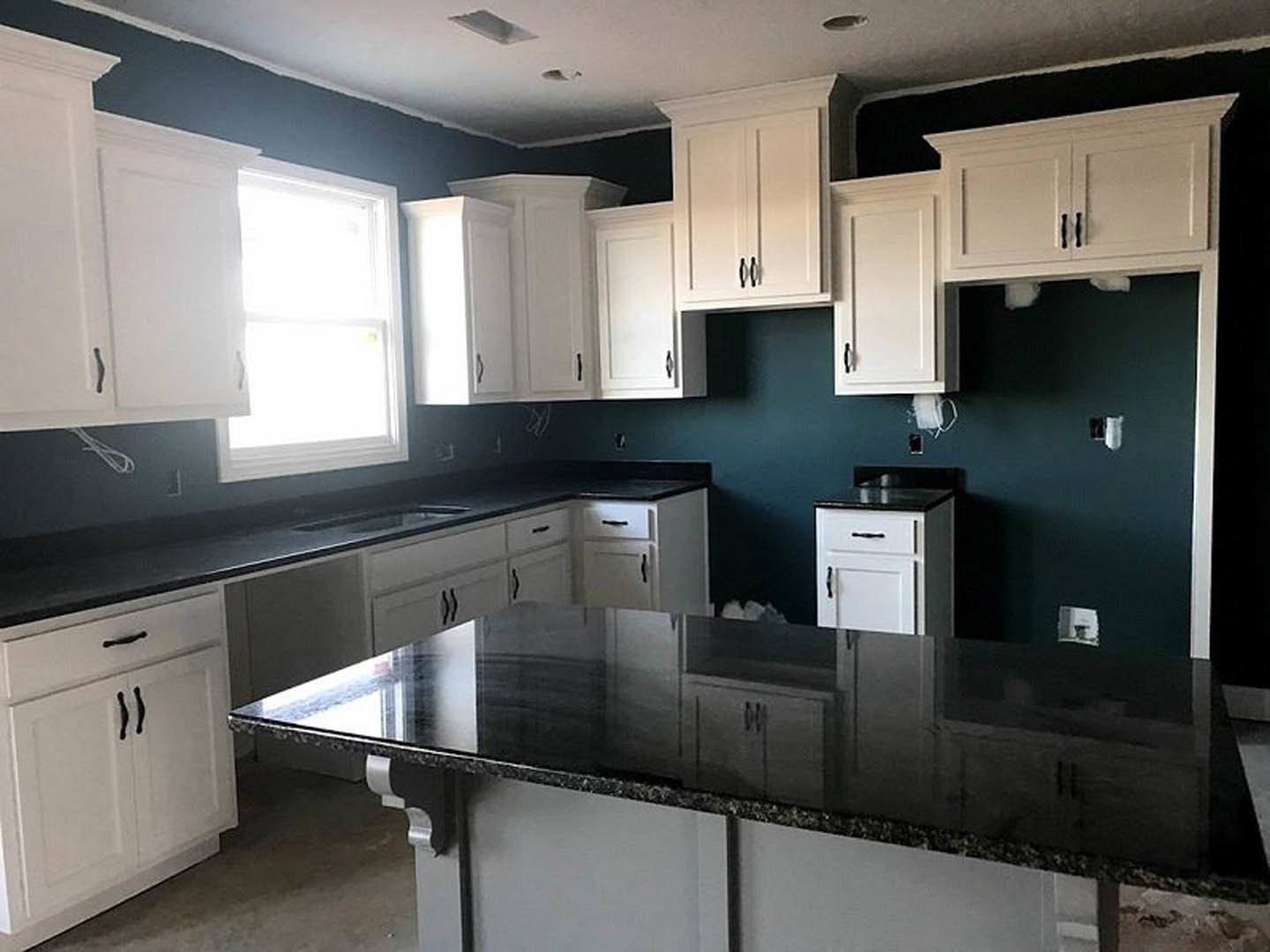 White kitchen cabinets with black countertops, stainless steel sink, and sunlight streaming through a window onto the workspace.