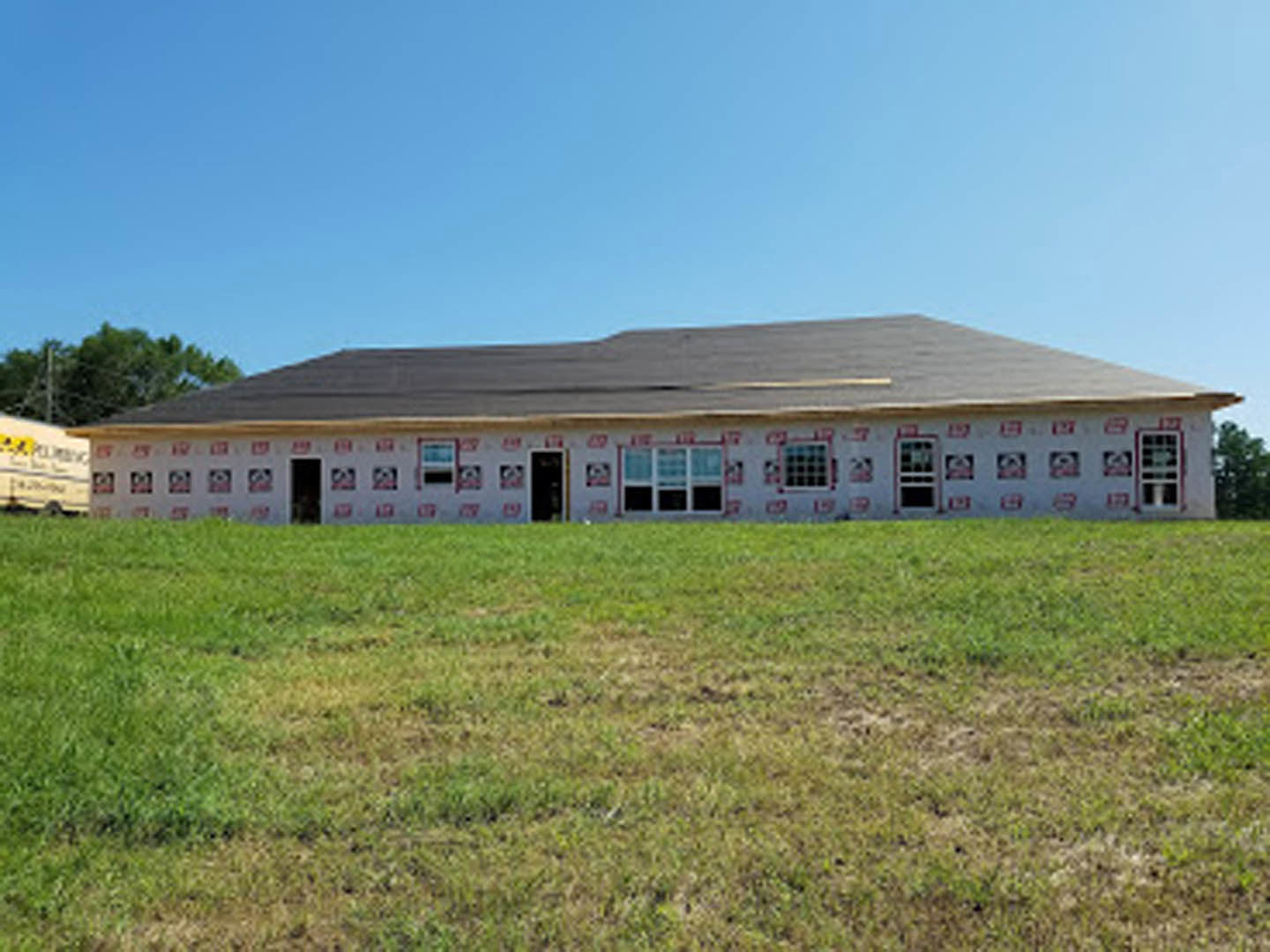 Modern two-story home with black-framed windows, open front door, and expansive green lawn bordered by trees under a clear sky