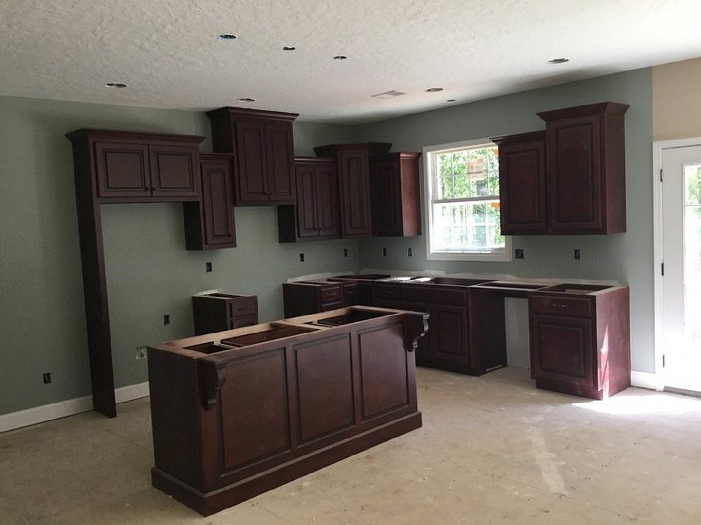 Kitchen featuring dark wood cabinets, matching drawers, white door with black handle, window displaying a red sign, black appliance on white countertop, and light-colored flooring.