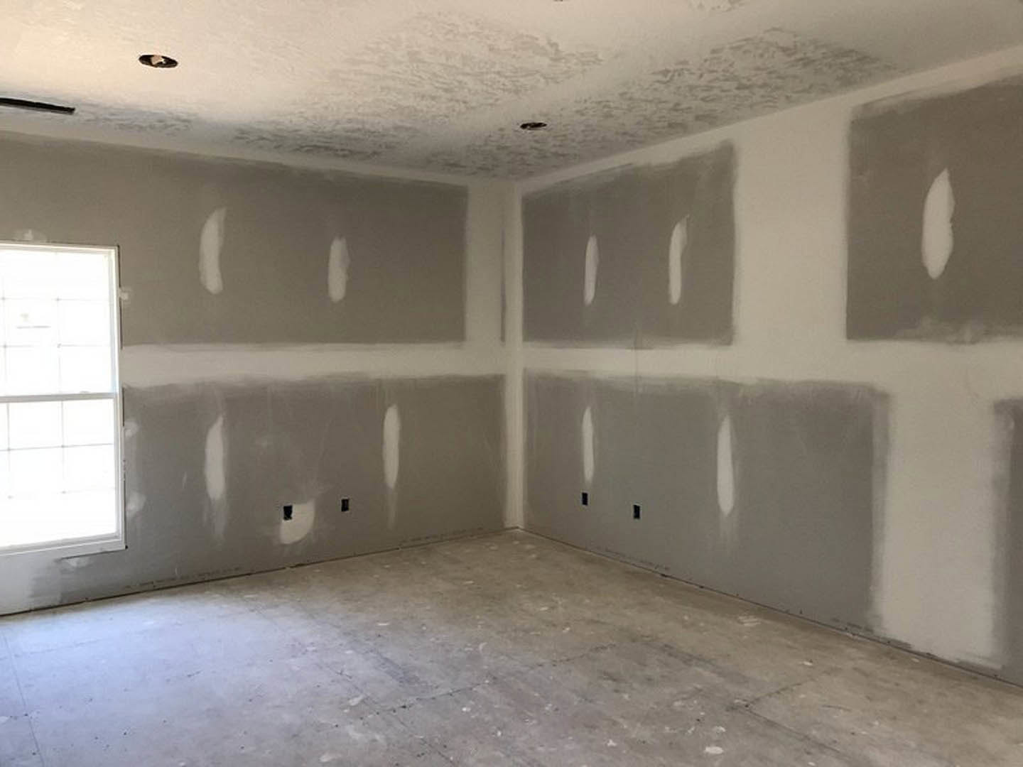 Room featuring white and gray plaster walls, gray flooring, white-framed window, and a white object with a black stripe; partial close-up of a person's face and a small white spot