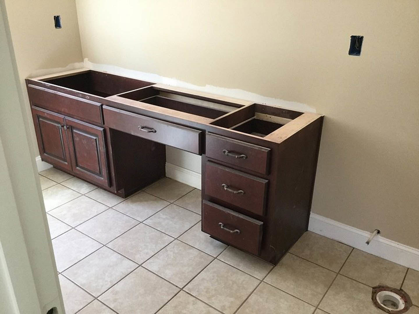 Light wood kitchen counter with multiple drawers, white tile backsplash, circular cutout in countertop, adjacent cabinetry and tiled floor