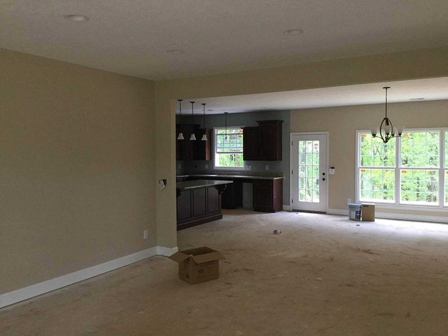 Open-concept kitchen with white cabinetry, light wood flooring, glass-paneled door, large window, and modern pendant light fixture