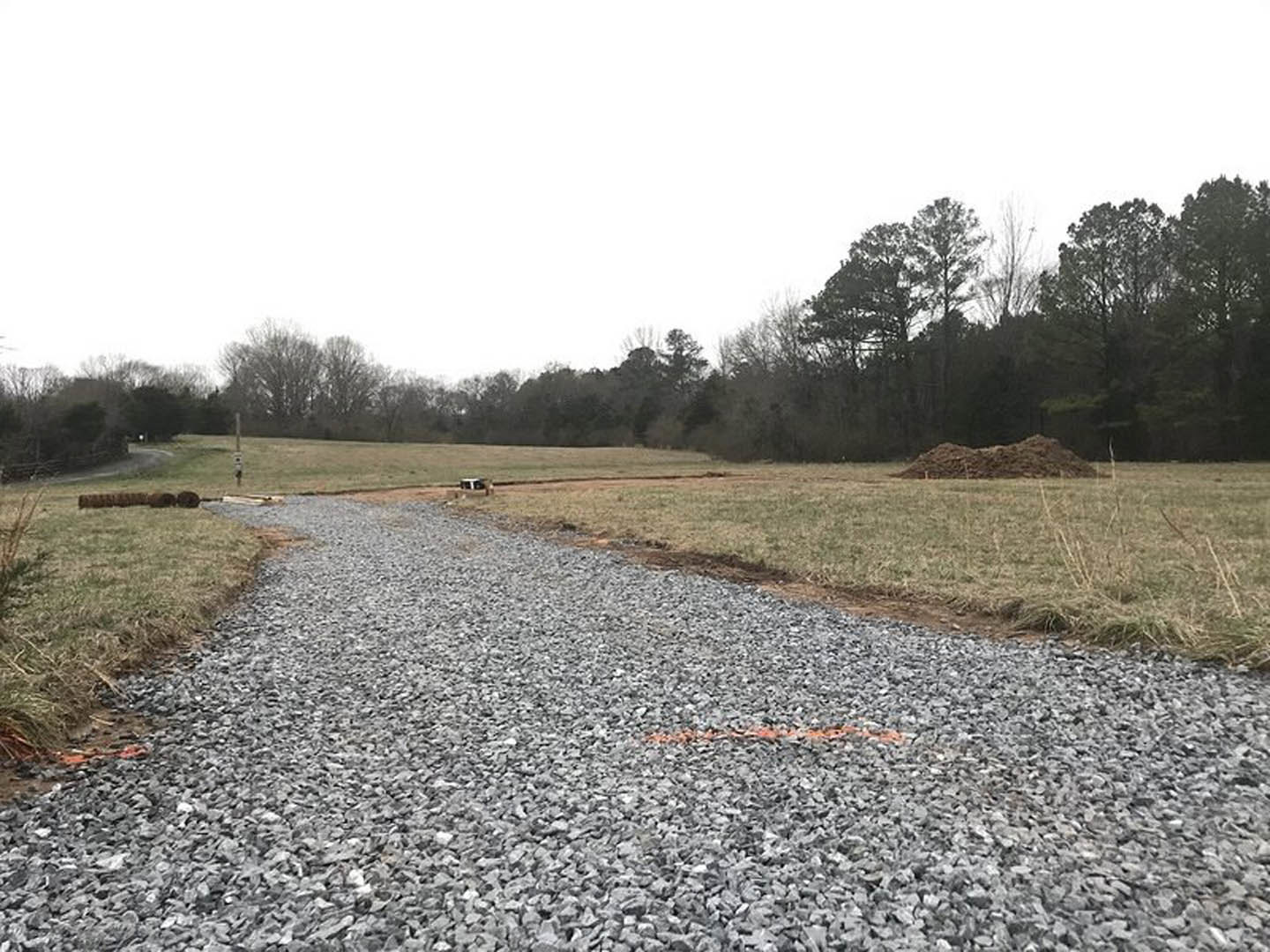 Gravel driveway bordered by green grass and mature trees under a clear sky