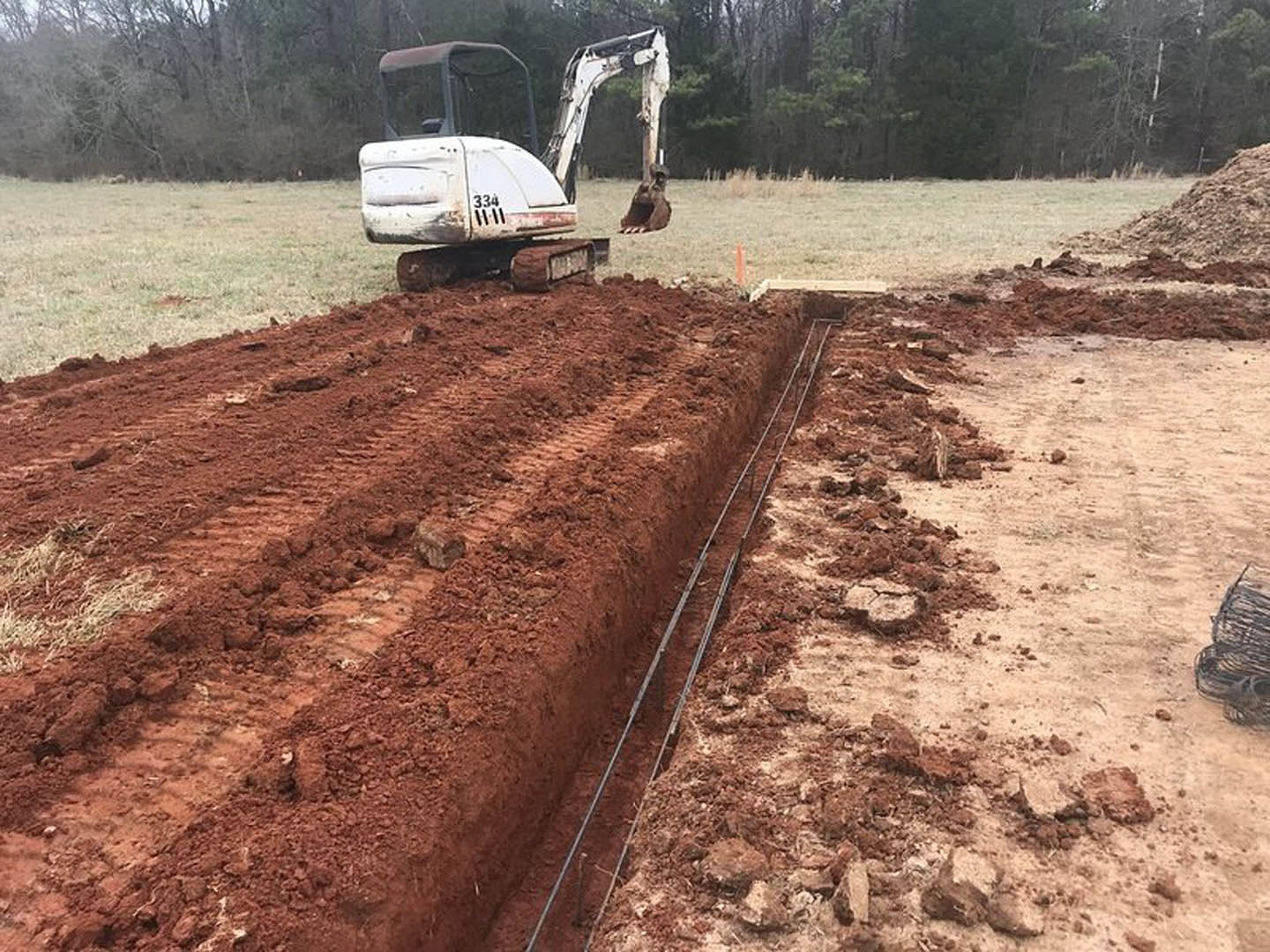Bulldozer digging a trench on a dirt construction site surrounded by trees and soil