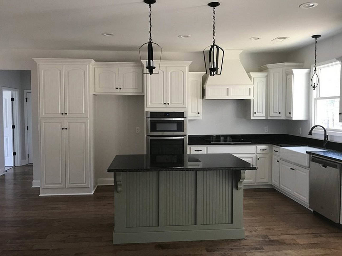 White kitchen cabinets with black countertops, built-in microwave, black cabinet knobs, stainless steel sink, pendant light fixture near a window.