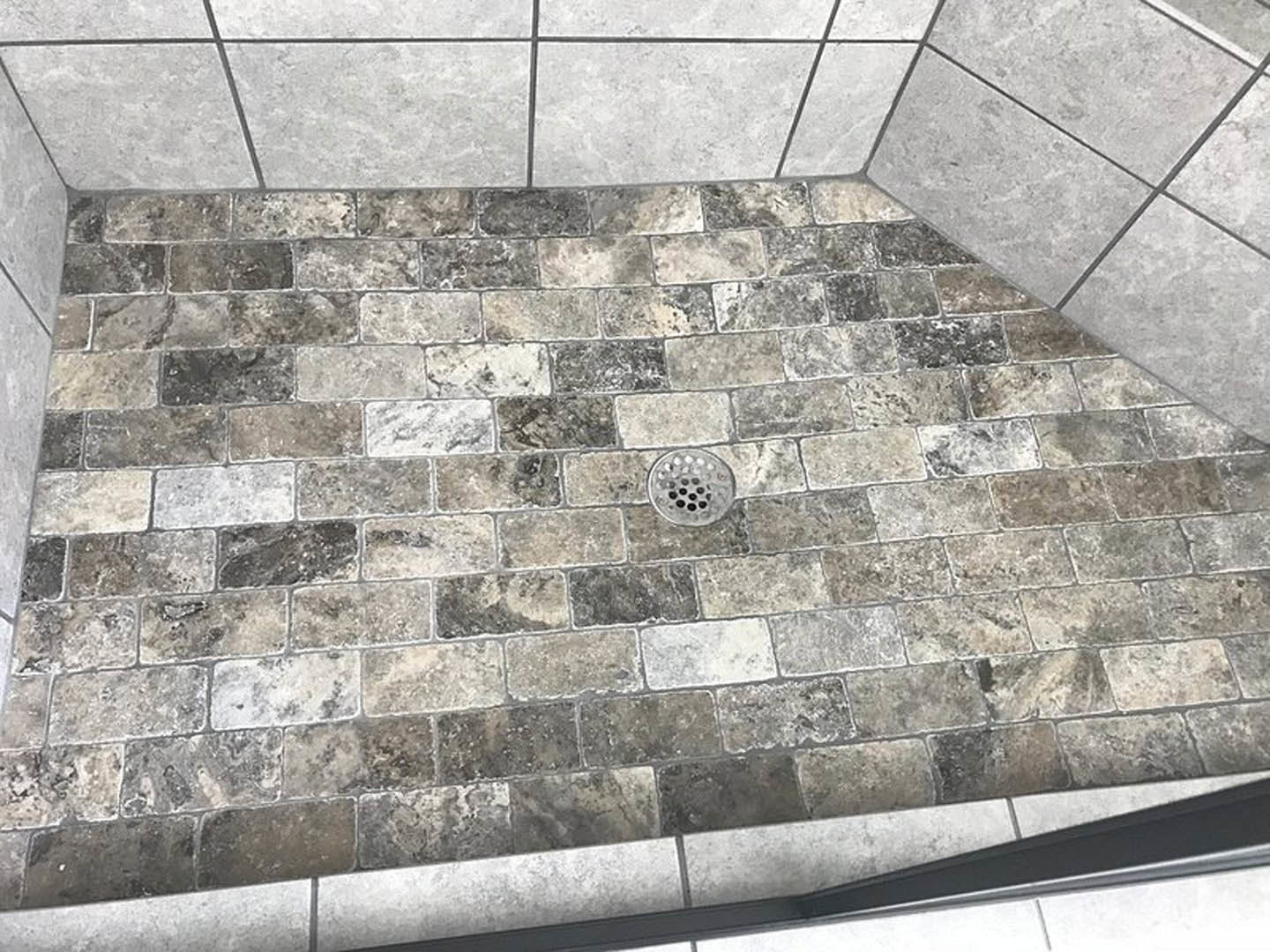 Rectangular tile shower floor with central metal drain, stone tile walls, and marble-like finishes