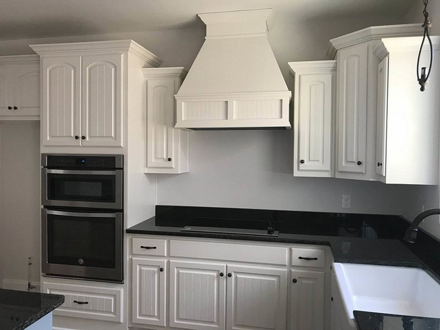 White kitchen cabinets with black countertops, black cabinet handles, built-in microwave, white vent hood, and white tub with black trim