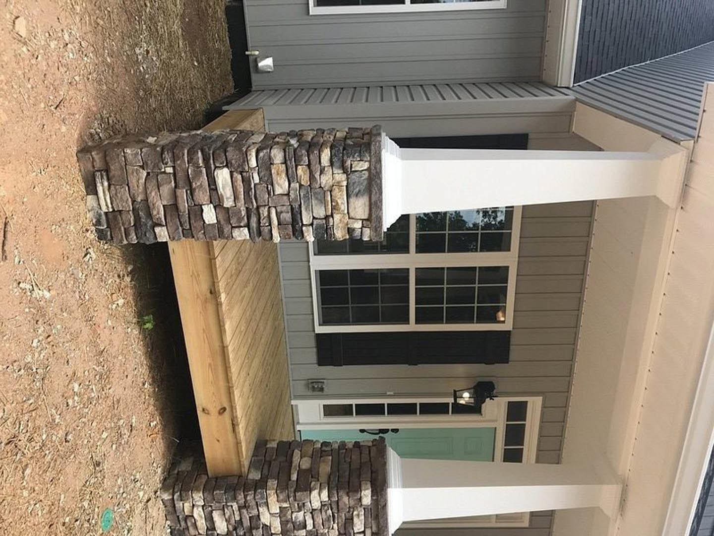 Stone columns supporting a front porch with stacked stone walls, green door with black trim, window framed by stone, and white shelf visible near entry.
