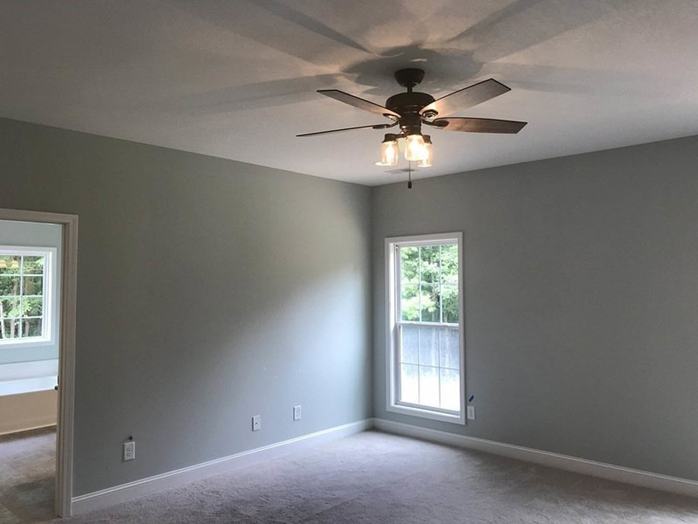 Ceiling fan with lights mounted on white plaster ceiling, multi-pane window with white frame, white carpeted floor, close-up view of paneled door, decorative wall molding
