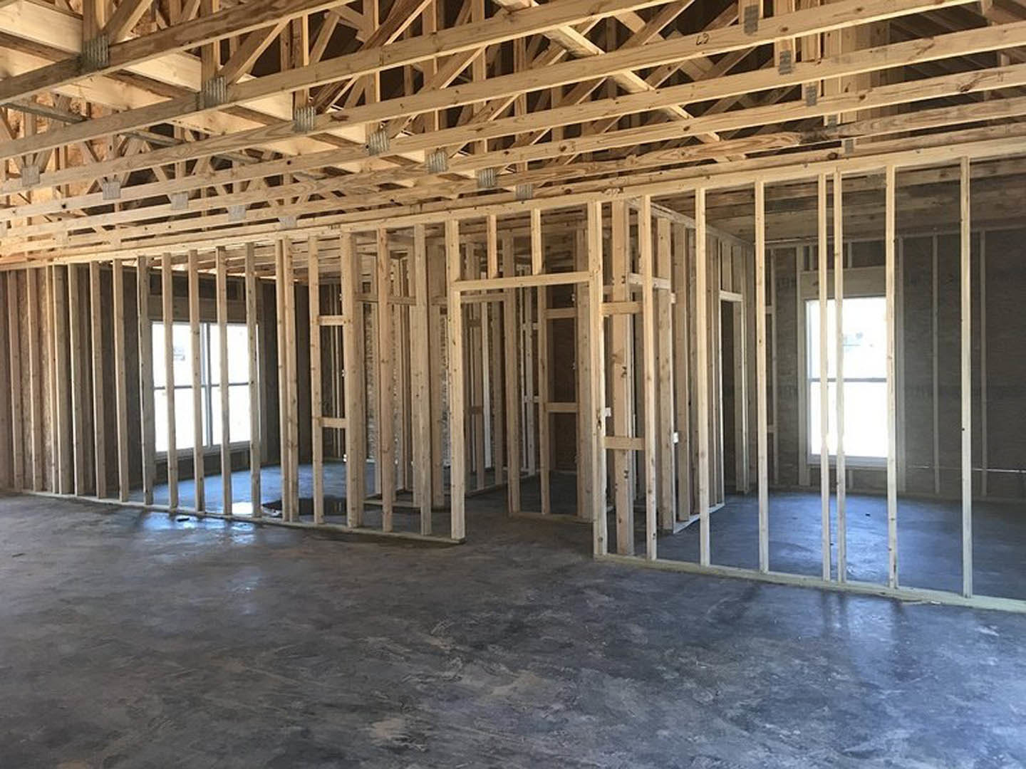 Wood-framed room with exposed beams, concrete floor, and sunlight streaming through a window