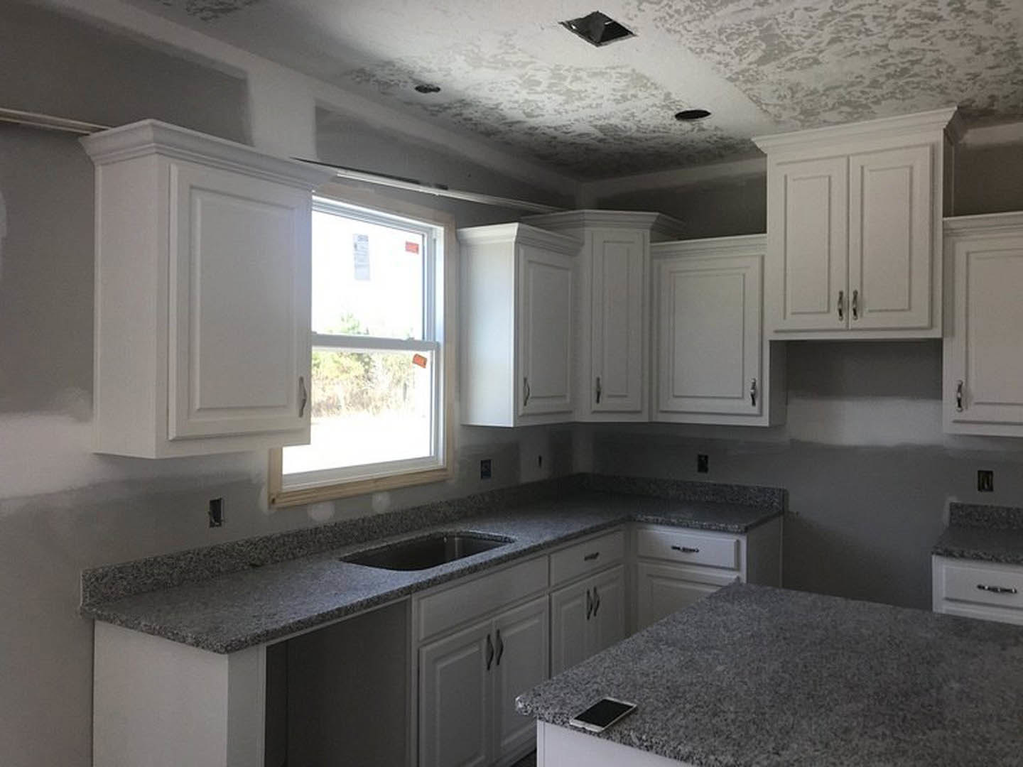 Granite countertops with white cabinetry, stainless steel sink, and kitchen appliances; window with signage in background
