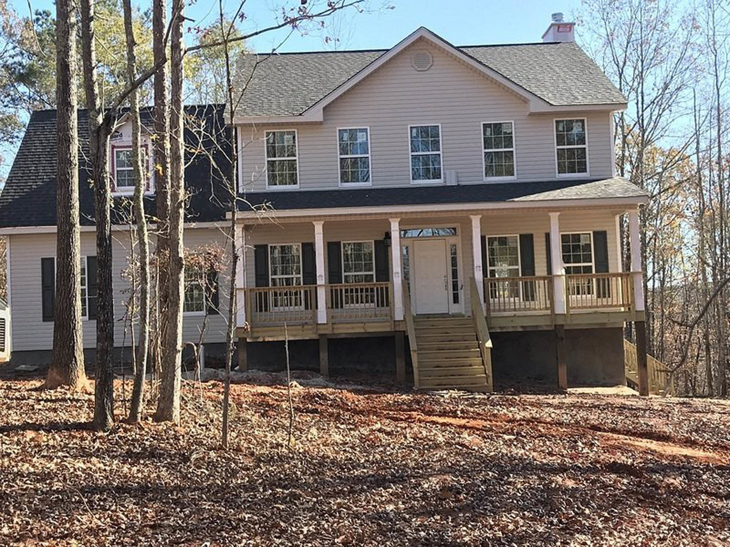 Two-story house with white siding, multiple-paned windows, covered front porch with wooden stairs, and a pile of leaves scattered on the ground.
