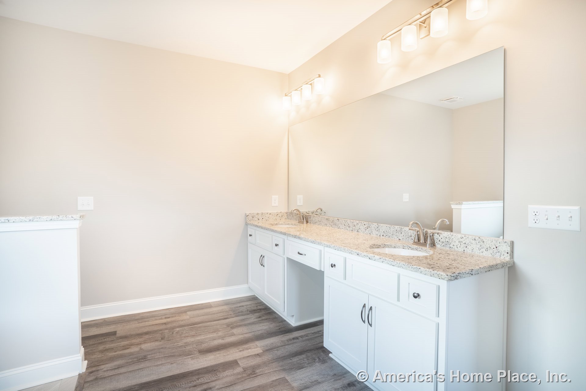 Long granite vanity with dual undermount sinks, white shaker cabinets, expansive wall-mounted mirror, modern vanity lighting, and wood-look vinyl flooring.
