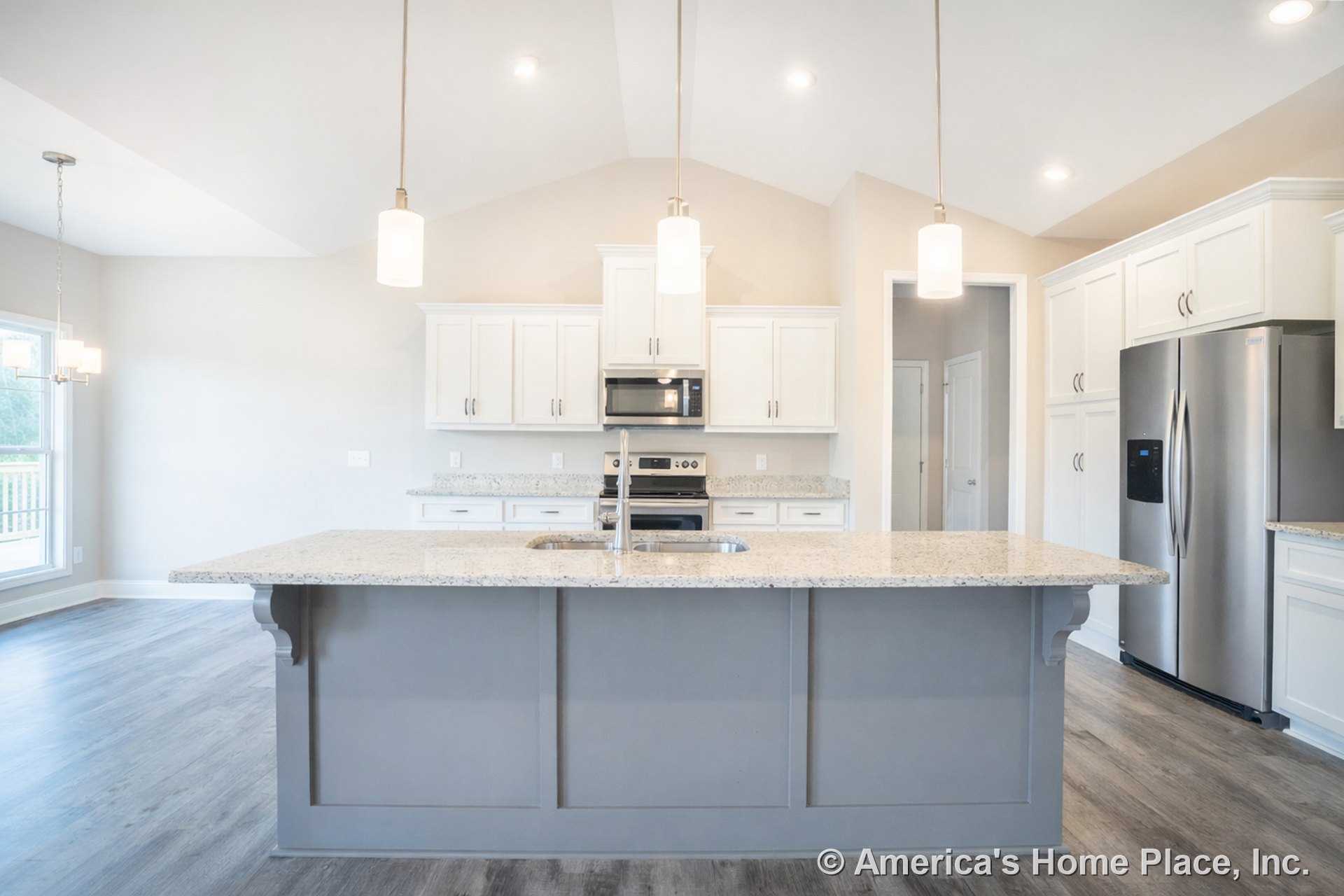 Spacious kitchen with vaulted ceiling, recessed lighting, and pendant lights above a large central island featuring granite countertops, white full-height cabinetry, stainless