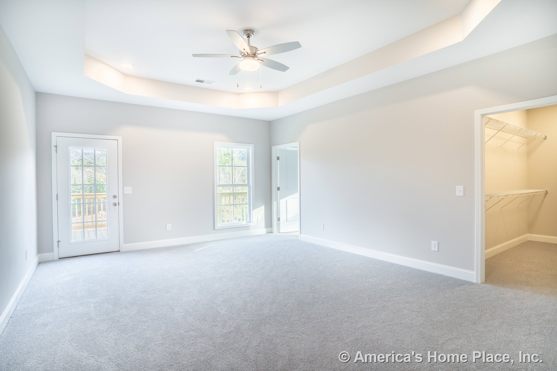 Tray ceiling with recessed lighting and ceiling fan, carpeted floor, double window with white trim, glass door opening to exterior deck, spacious walk-in closet with wire shelving