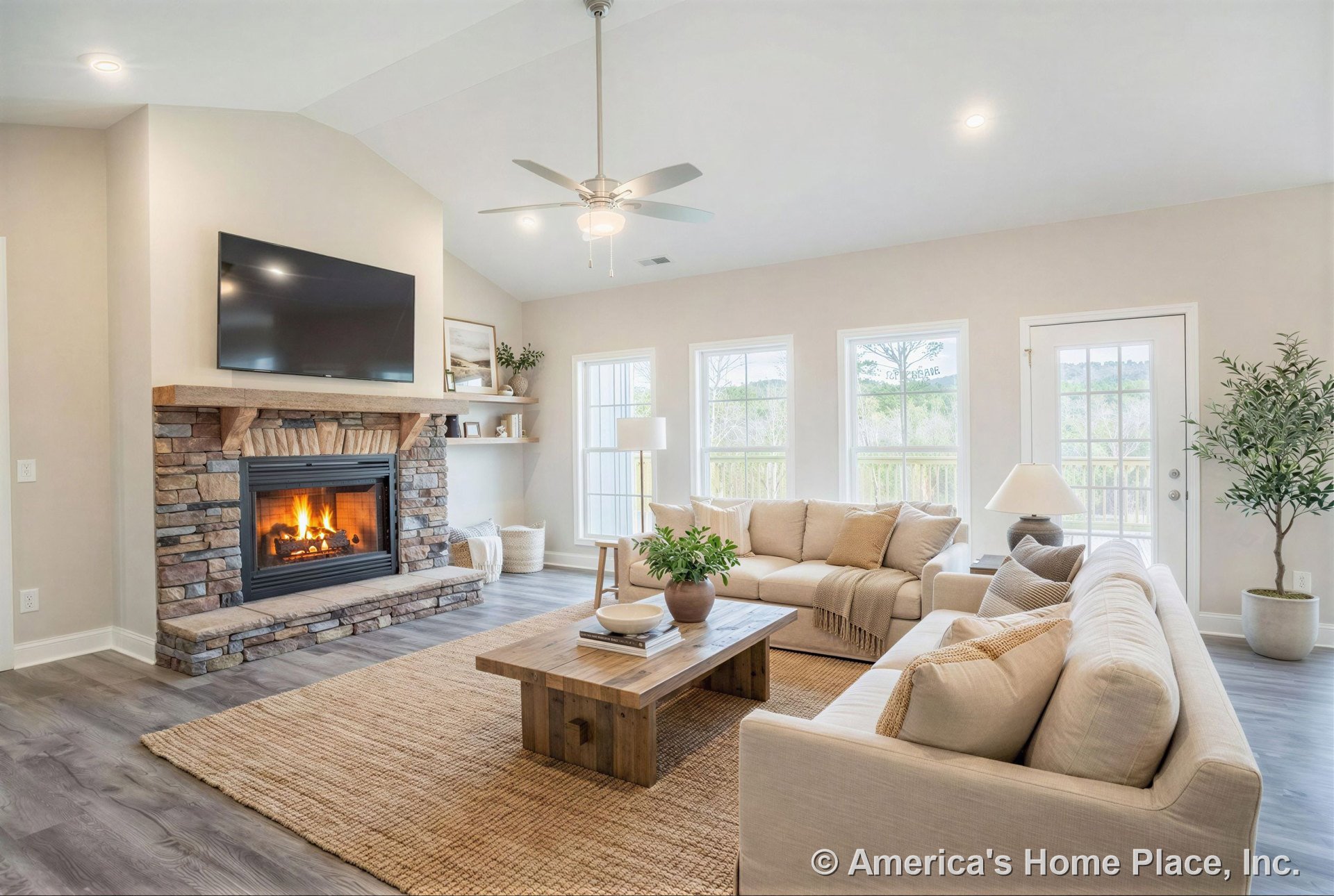 Stone fireplace with wood mantel, ceiling fan with built-in light, three large windows, glass exterior door, recessed ceiling lights, tray ceiling, built-in shelving, gray