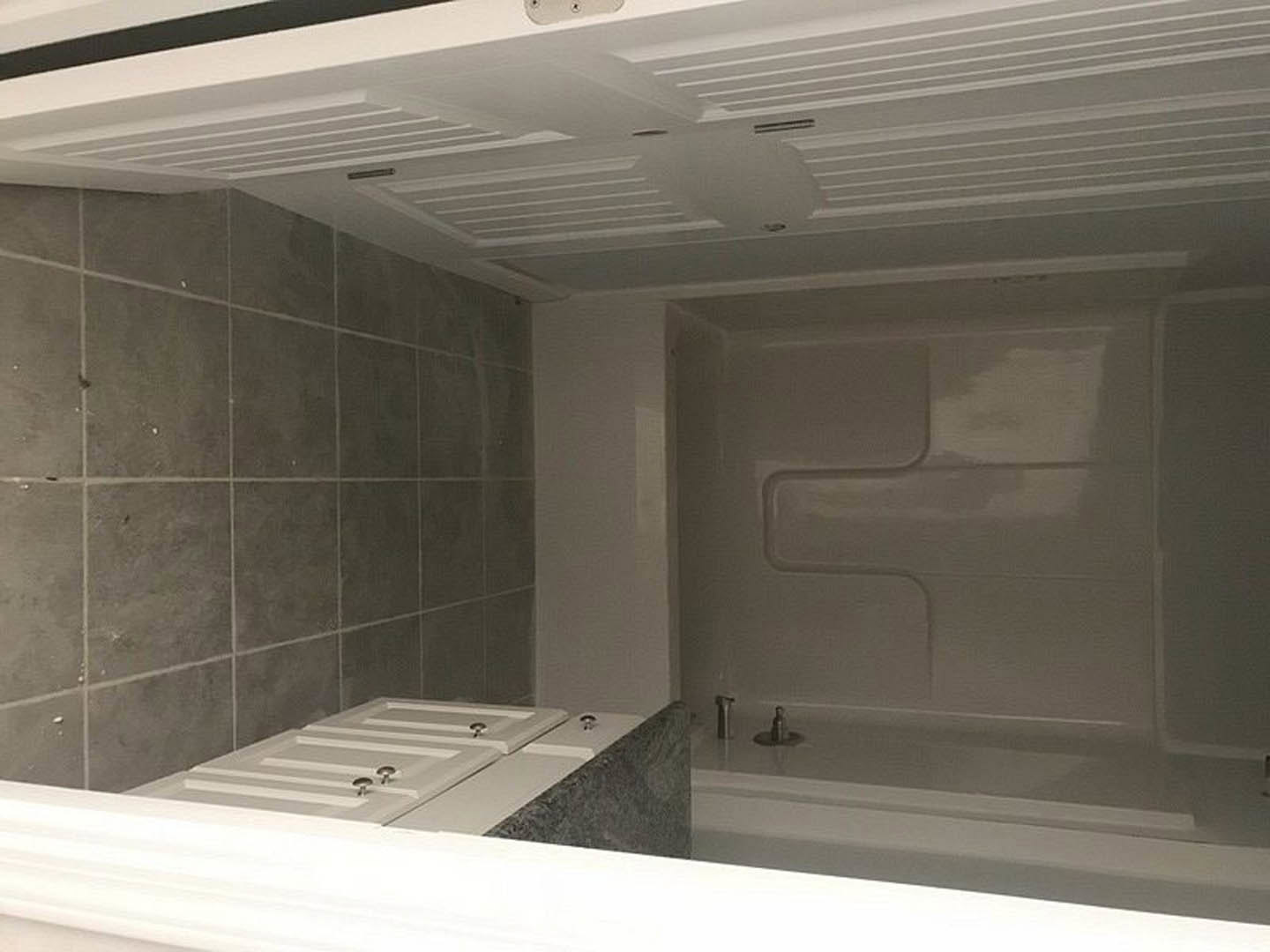 Bathroom with white tile shower, white vanity cabinet with silver knobs, white bathtub, and white sink; white door visible, neutral walls and ceiling.