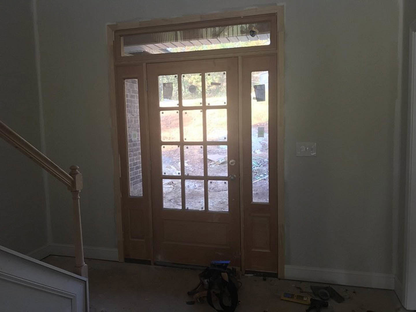 White door with glass panels, silver door handle, white railing, black backpack on light wood flooring, neutral walls in entryway.