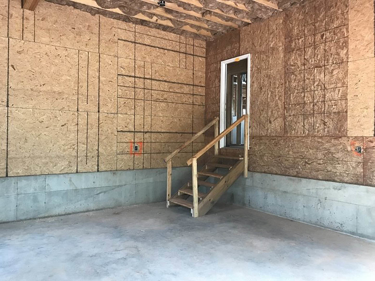 Wooden staircase with metal handrail beside exposed brick wall, concrete floor, and large window; person standing near window.