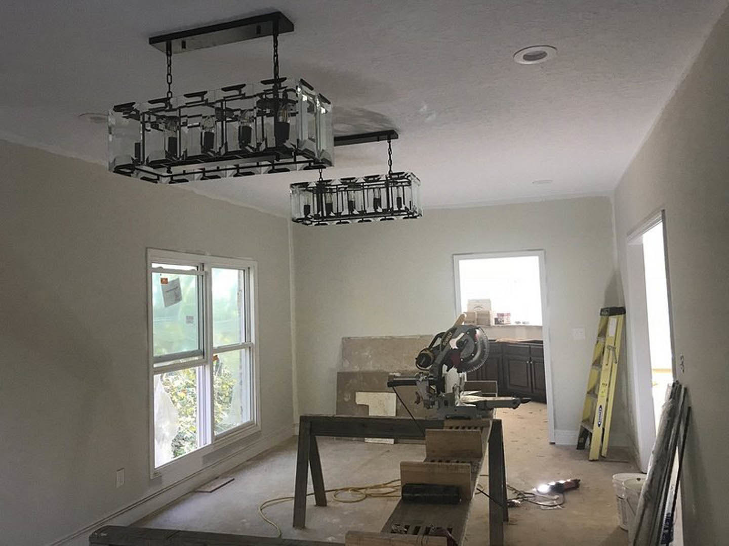 Unfinished room with plaster walls, ceiling fan, window, and construction materials including a saw and white paper with red label on floor