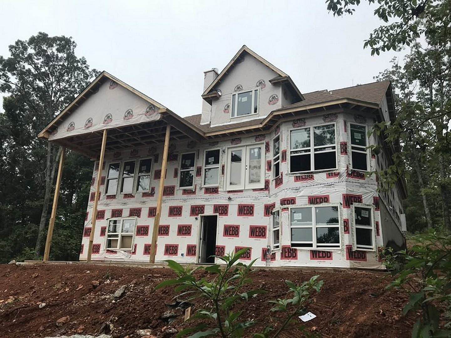 White siding house with red tape and black signs on exterior, visible windows, door, and nearby green plant.