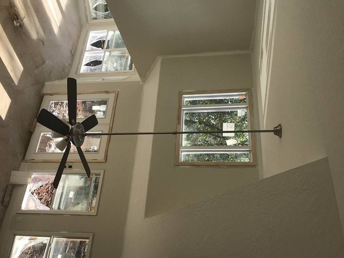 Ceiling fan with metal rod mounted on white plaster ceiling, large window with black striped trim, tree visible outside, close-up of door handle in modern residential room