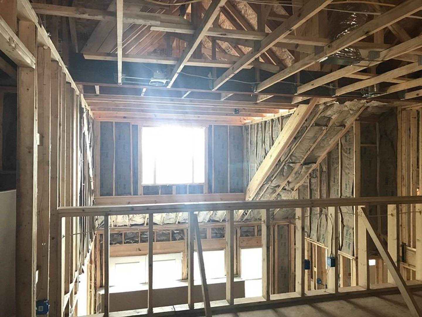 Sunlit room with exposed wooden ceiling beams, large window, white walls, and construction ladder.