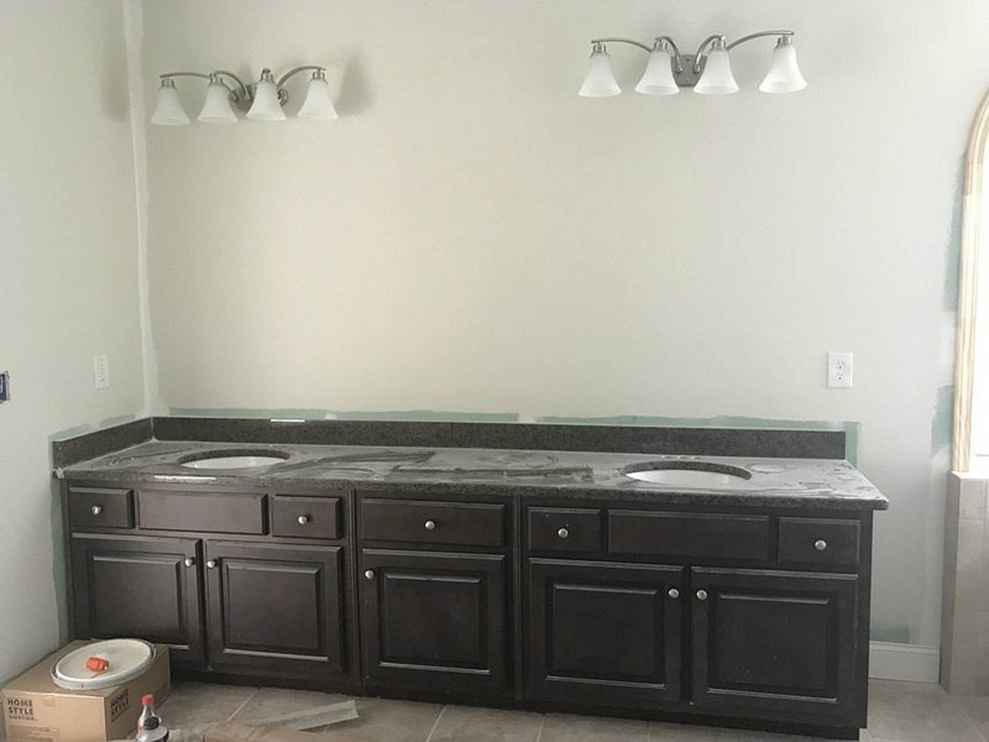 Bathroom with double sinks, white countertop and drawers, chrome faucets, tile backsplash, two white globe light fixtures above mirror, decorative bottle on vanity.