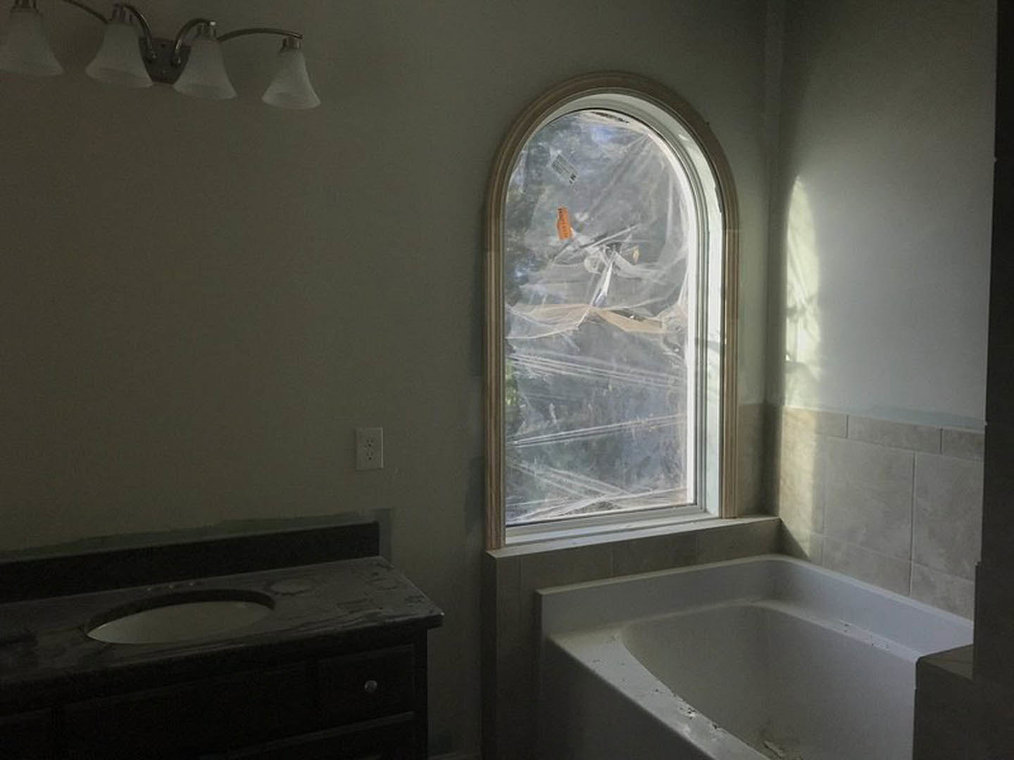 Modern bathroom featuring a freestanding bathtub, white sink with chrome faucet, large window, wall-mounted mirror, and light-colored tile walls