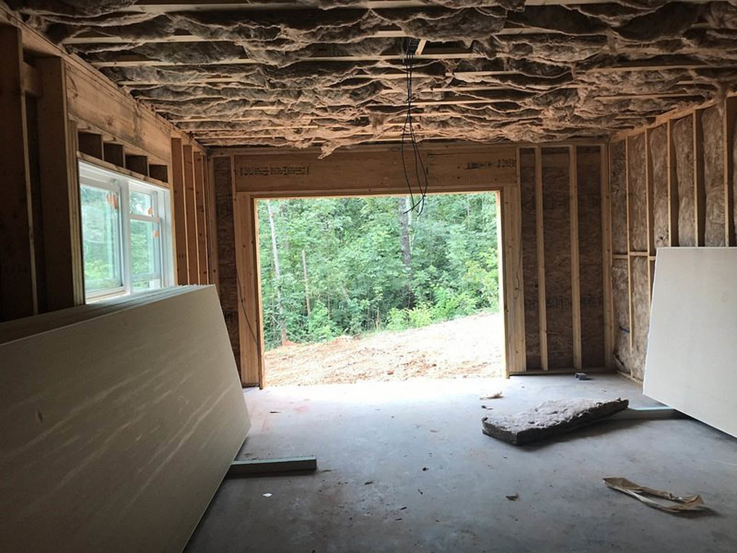 Room with a white-framed window overlooking trees, exposed rock ceiling, large wooden beam, and white wall surface