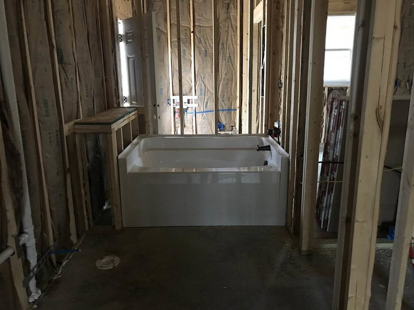 Freestanding white bathtub with chrome fixtures beside a wood accent wall, light plaster walls, and dark tile flooring in a modern bathroom