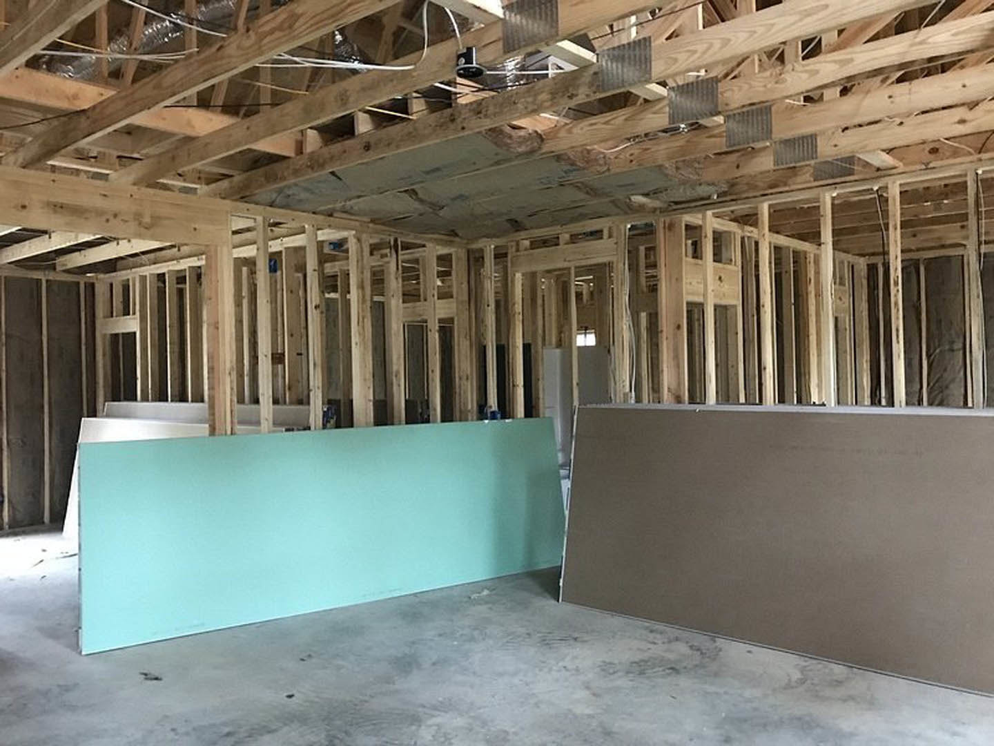 Blue accent wall with wooden ceiling beams, grey concrete floor, recessed vent, and modern light fixture in a residential interior.