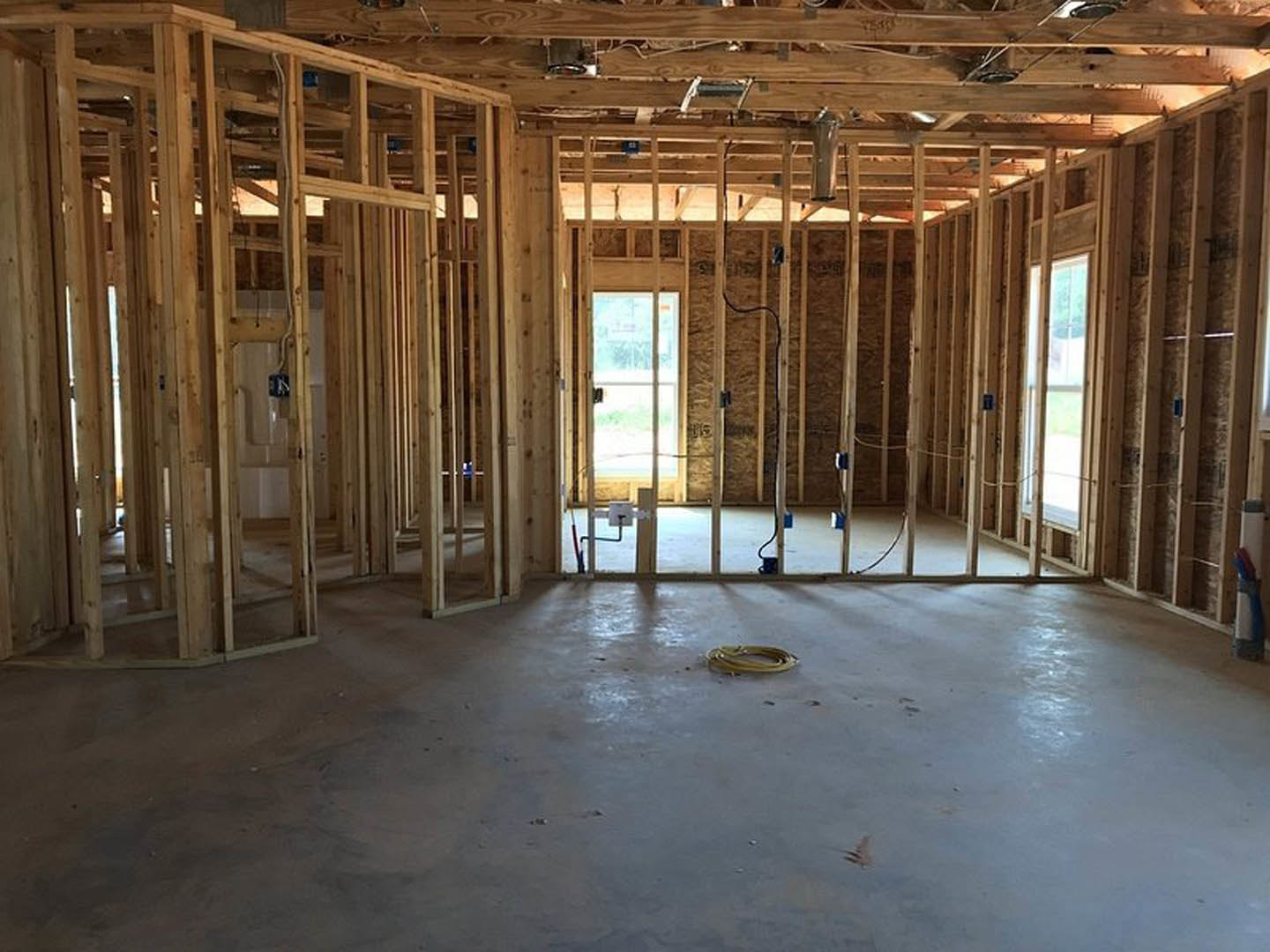 Unfinished room with exposed wood framing, ceiling beams, building insulation, and a yellow hose lying on the floor