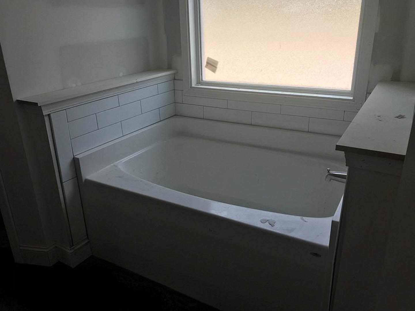 Freestanding white bathtub with chrome faucet beside large window, light gray tile floor, and pale walls in modern bathroom