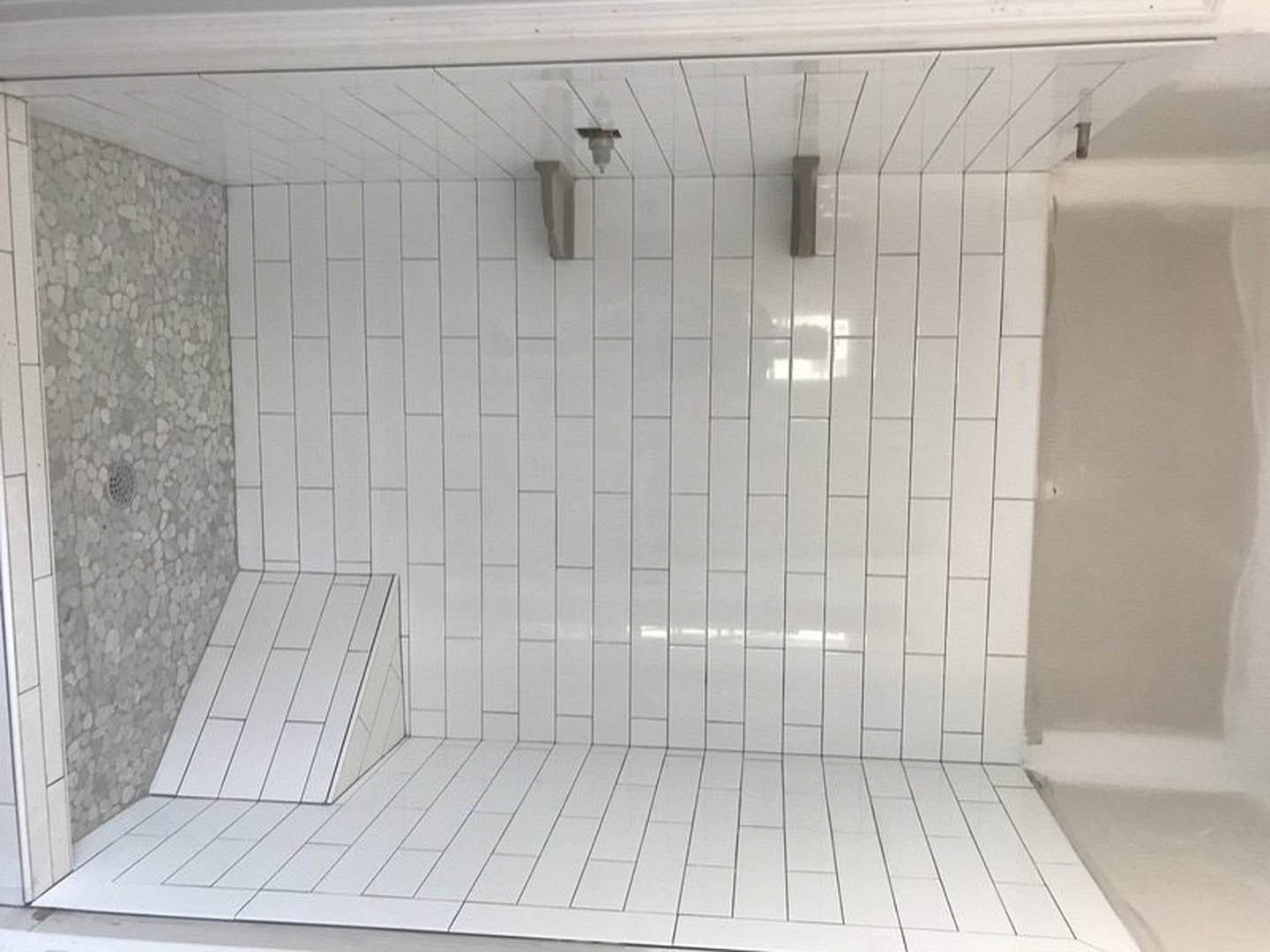White tiled shower floor with central drain, marble tile walls, and glass door visible in modern bathroom.