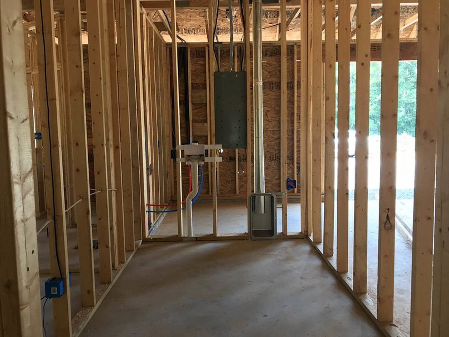 Unfinished room with exposed wood framing, concrete floor, window, electrical box with wires, and construction materials