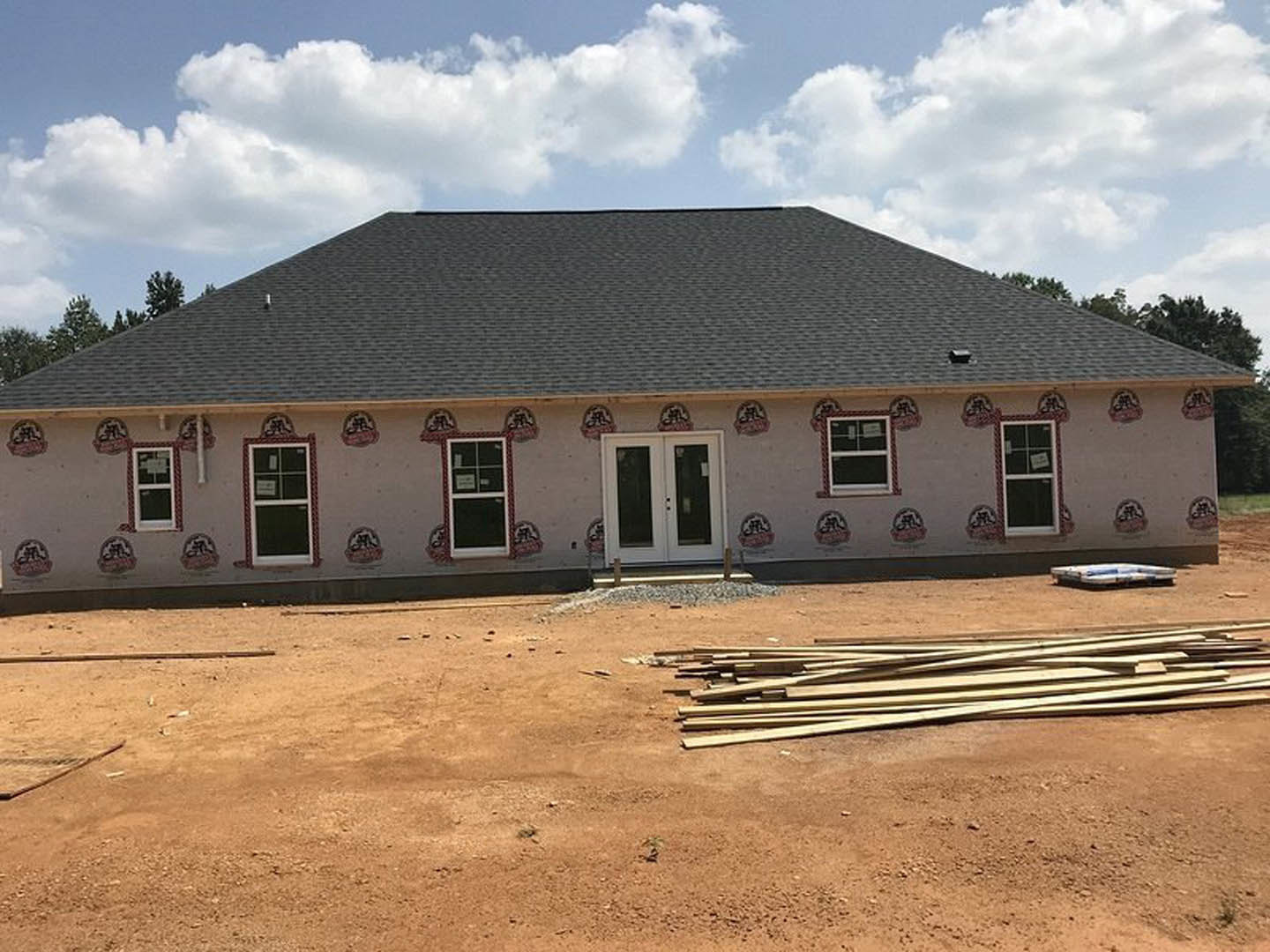 Two-story home under construction with double glass doors, white-framed windows, and a large pile of lumber on dirt in the front yard