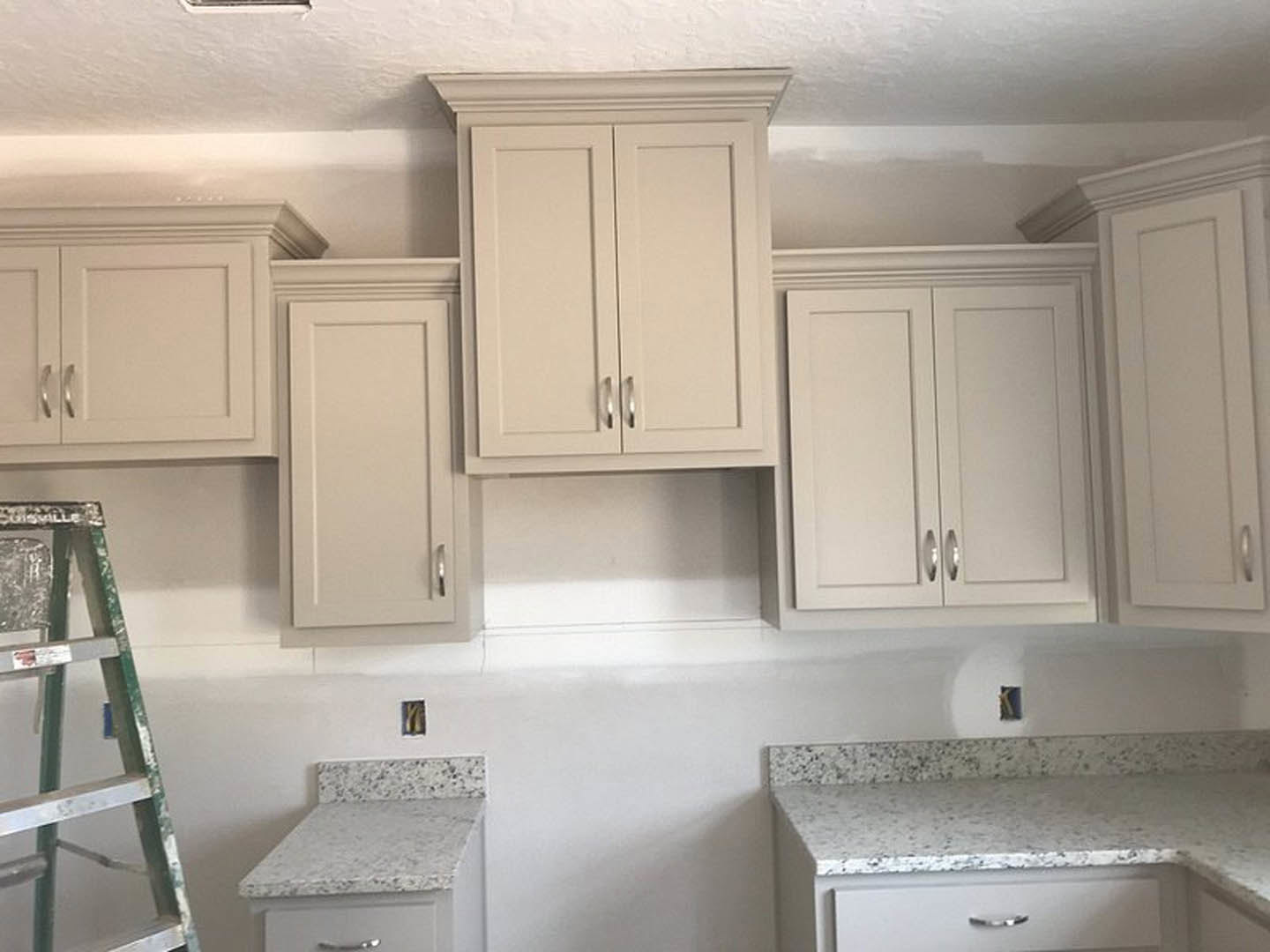 Modern kitchen featuring white cabinets with silver handles, white countertops, stainless steel sink, and a step ladder with paint marks positioned near the cabinetry.