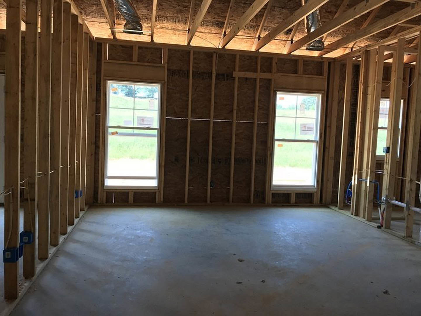 Room with large windows, exposed wooden ceiling beams, concrete floor, and a window featuring a sign; blue box visible in the background.