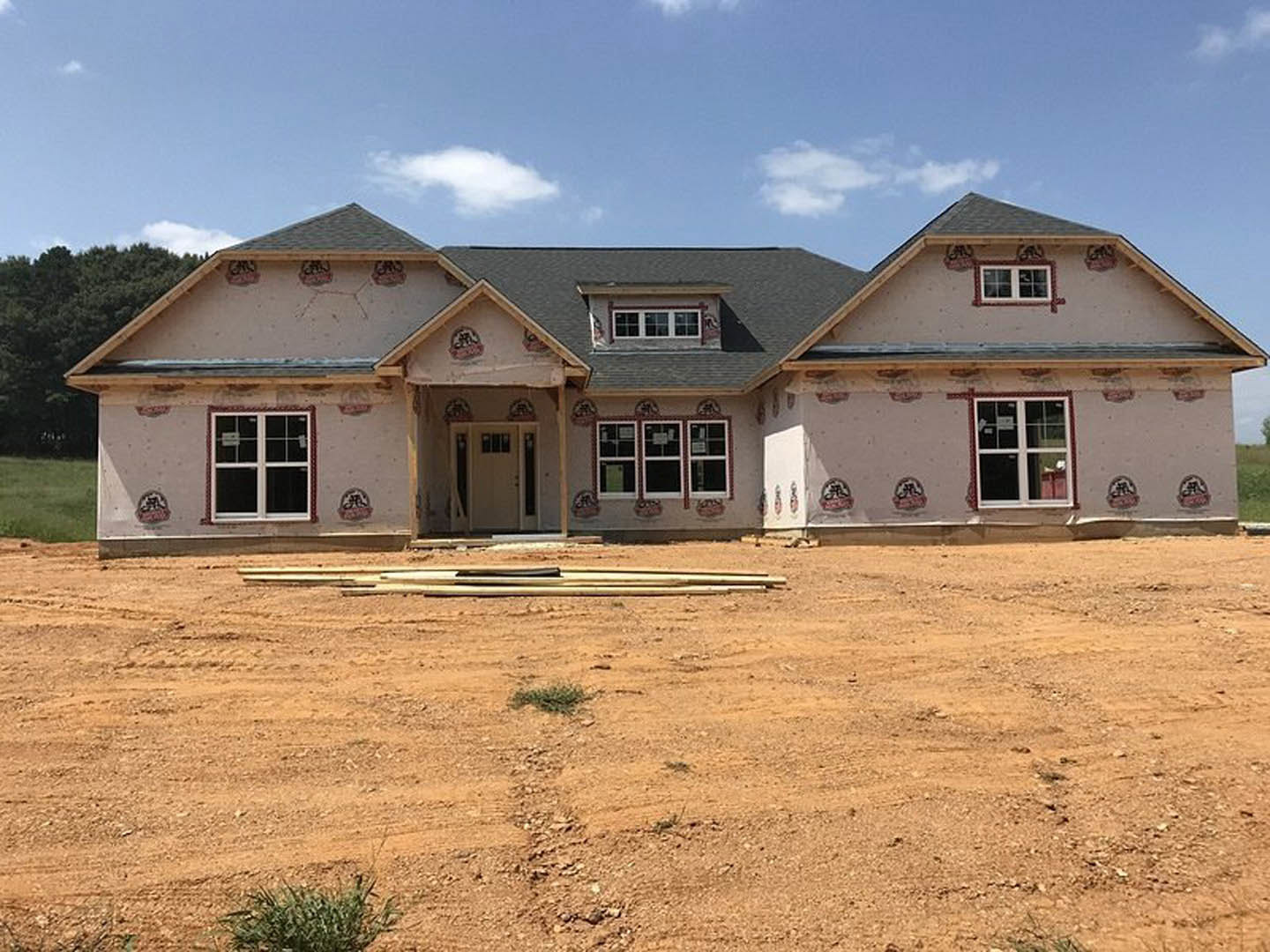 Framed house under construction with exposed wood, dirt lot in foreground, and clear blue sky overhead